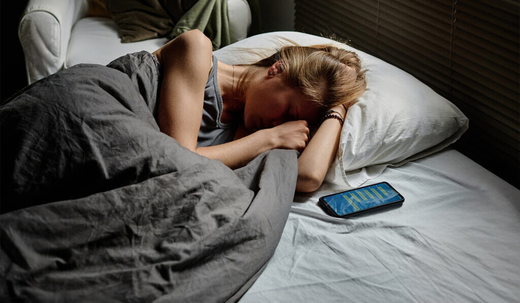 A upset woman lying in bed with her phone beside her.