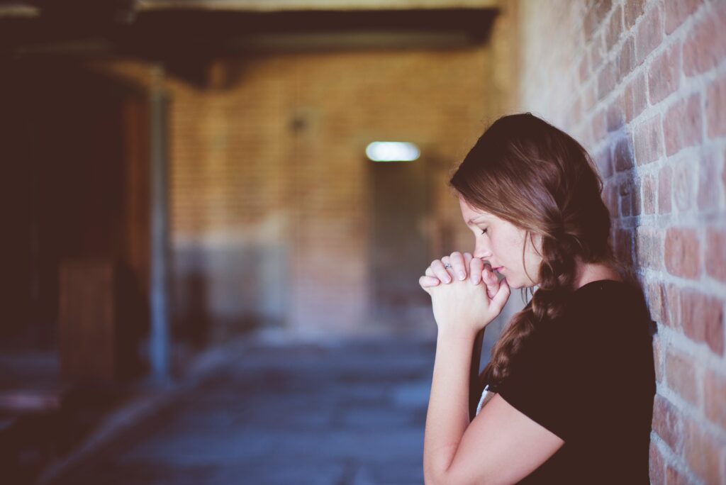 Woman praying while leaning against a brick wall