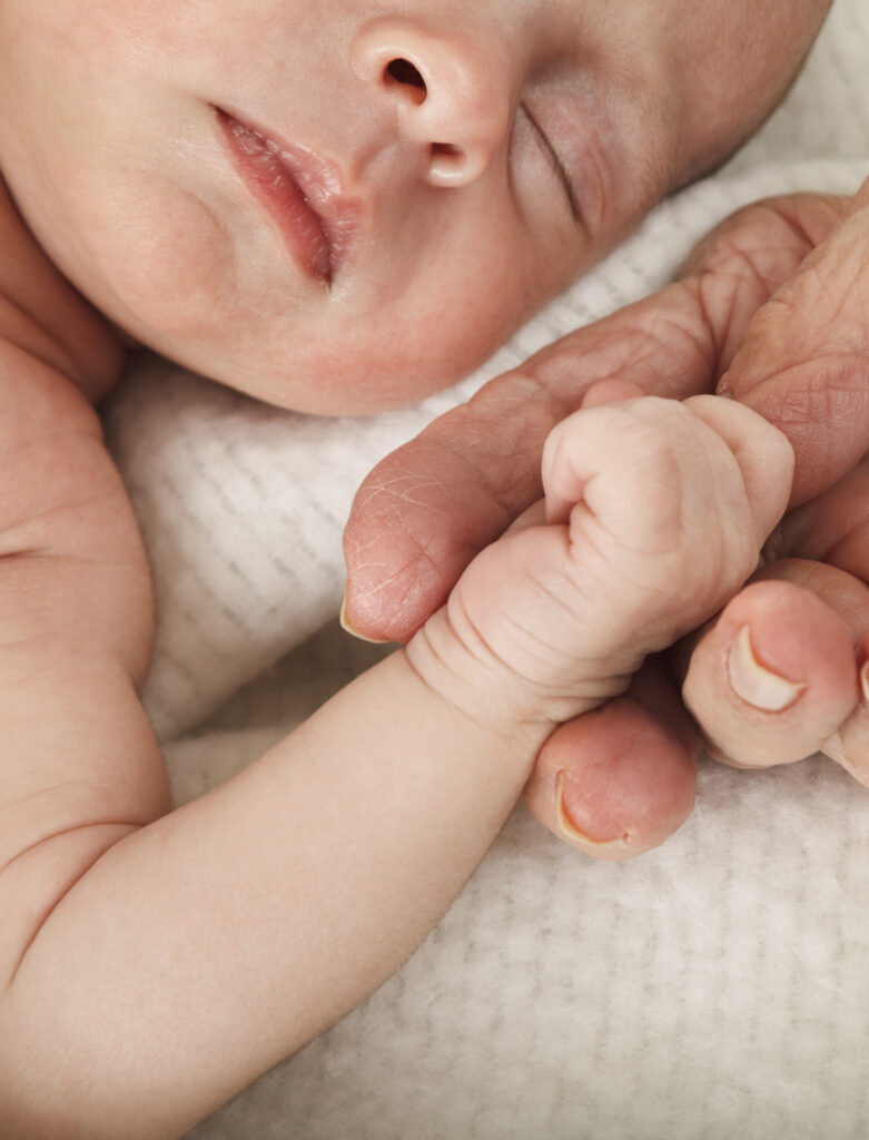 An adult hand holding the hand of a baby.