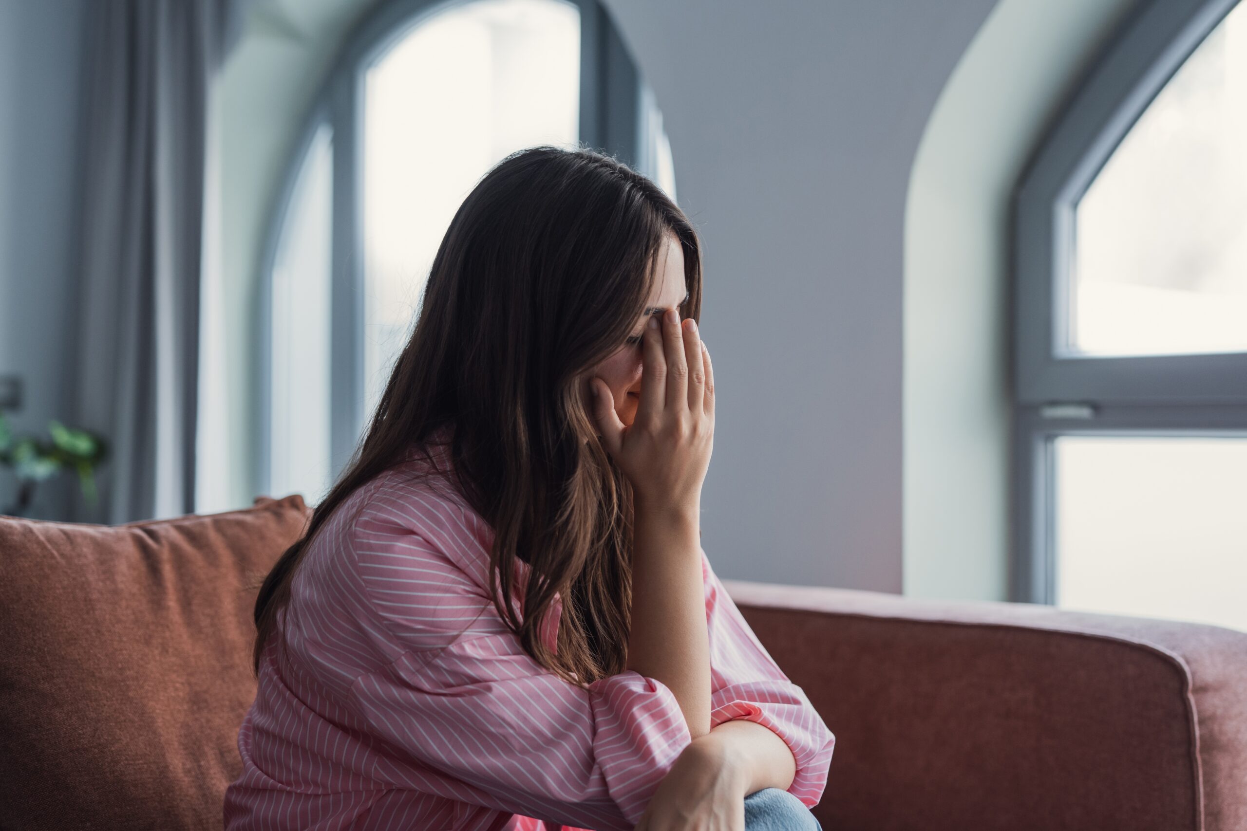 Close-up of a sad young woman sitting alone at home, lost in thought about personal problems.