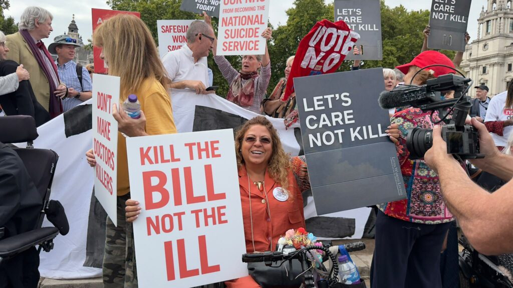 Protesters hold signs opposing assisted-dying legislation at a public demonstration